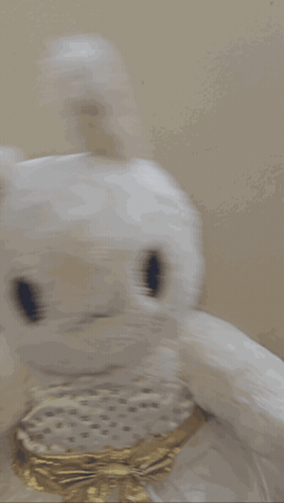 A White Stuffed Bunny With A Gold Bow On Its Neck GIF