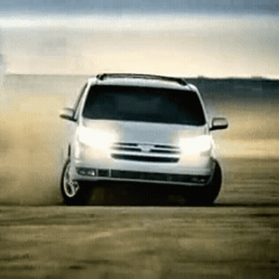 A White Suv Is Driving On A Dirt Road With Its Lights On GIF