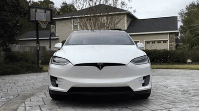 A White Tesla Is Parked In A Driveway In Front Of A House GIF