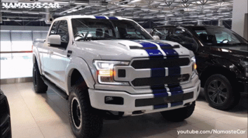 A White Truck With A Blue Stripe On The Front Is Parked Next To A Black Car GIF