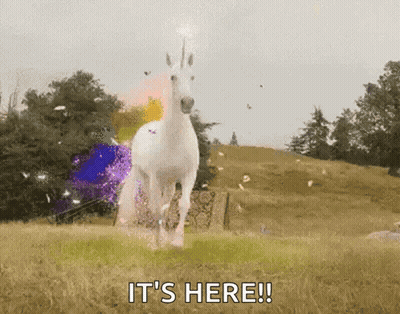 A White Unicorn Is Running In A Field With The Words It 'S Here Written Below It . GIF