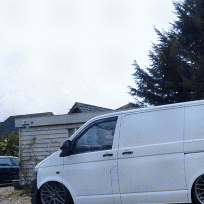 A White Van Is Parked In Front Of A Building With A Cross On It GIF