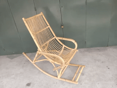 A Wicker Rocking Chair Sits On A Cement Floor In Front Of A Green Door GIF