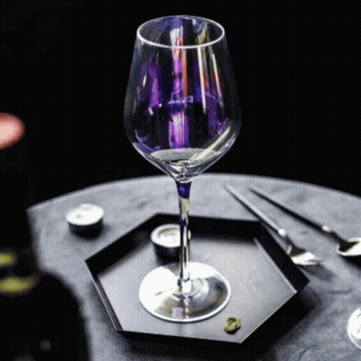 A Wine Glass With A Purple Stem Is Sitting On A Black Plate On A Table . GIF