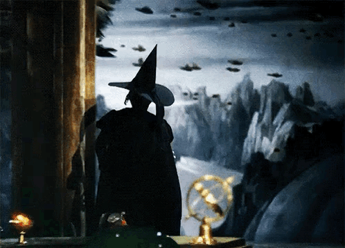 A Witch In A Witch Hat Stands In Front Of A Painting GIF