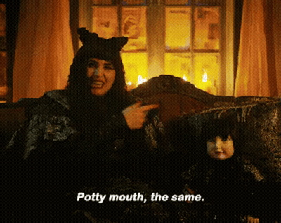 A Witch Is Sitting On A Couch Next To A Doll And Pointing At It . GIF