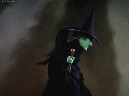 A Witch With Green Face And A Black Hat Holding A Cane GIF
