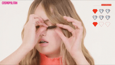 A Woman Adjusts Her Eyelashes In Front Of A Scoreboard With Diamonds GIF