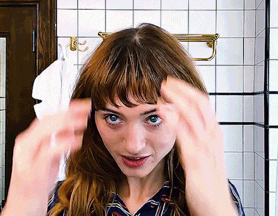 A Woman Adjusts Her Hair In A Bathroom With A Towel Hanging On The Wall GIF