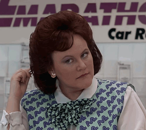 A Woman Adjusts Her Hair In Front Of A Marathon Car Rental Sign GIF