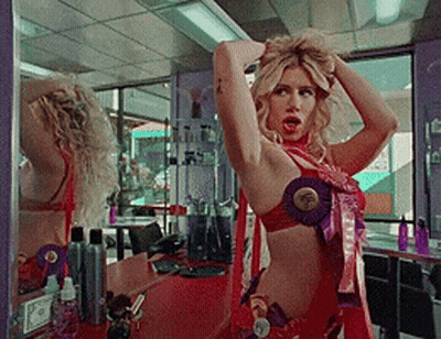 A Woman Adjusts Her Hair In Front Of A Mirror In A Beauty Salon GIF