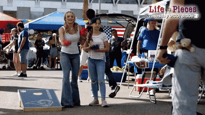 A Woman And A Girl Are Playing A Game Of Cornhole At A Life In Pieces Event GIF