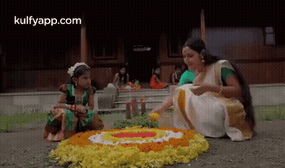 A Woman And A Little Girl Are Sitting On The Ground Making A Floral Arrangement . GIF