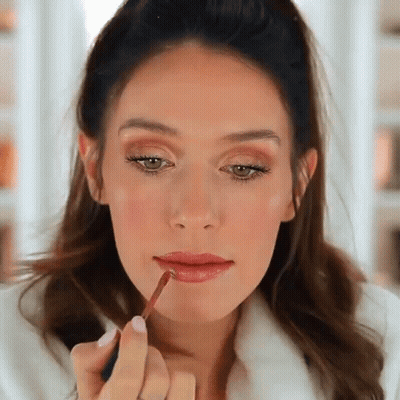 A Woman Applying Lip Gloss To Her Lips With A Brush GIF