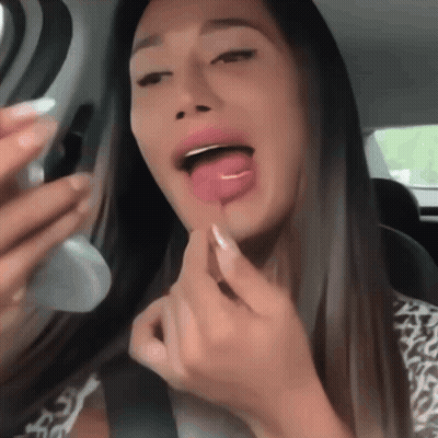 A Woman Applying Lipstick In A Car With Her Tongue Sticking Out GIF