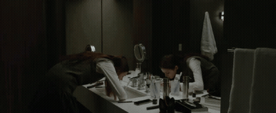 A Woman Applying Makeup In Front Of A Mirror In A Bathroom GIF