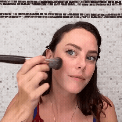 A Woman Applying Makeup With A Brush On Her Face GIF