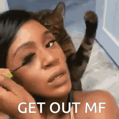 A Woman Applying Mascara With A Cat Behind Her And The Words Get Out Mf On The Bottom GIF