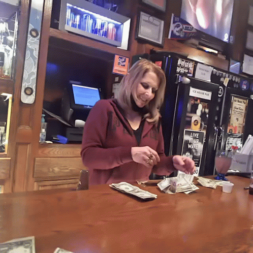 A Woman At A Bar With A Sign That Says " Live The Wave " GIF