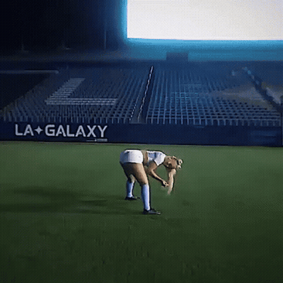 A Woman Bending Over On A Soccer Field In Front Of A La Galaxy Banner GIF