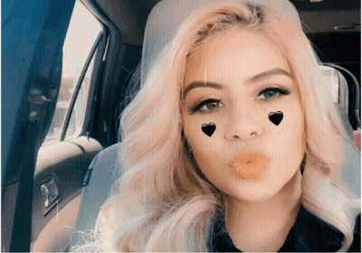 A Woman Blowing A Kiss With Hearts On Her Face In A Car GIF