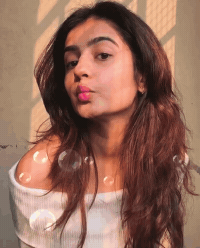 A Woman Blowing Bubbles In Front Of Her Face GIF