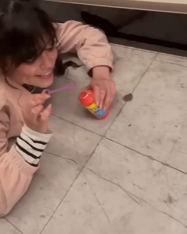 A Woman Blowing Soap Bubbles On The Floor With A Can Of Bubbles GIF