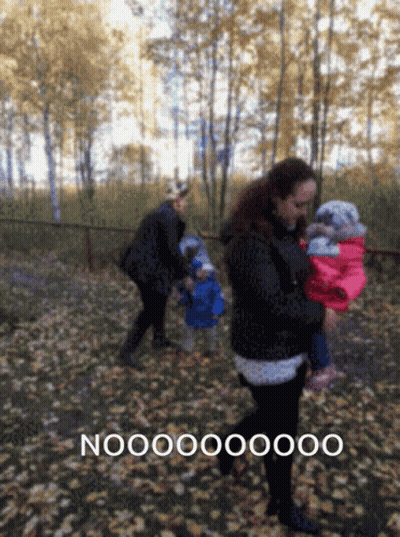 A Woman Carrying A Baby In A Park With The Word Nooo On The Bottom Left GIF