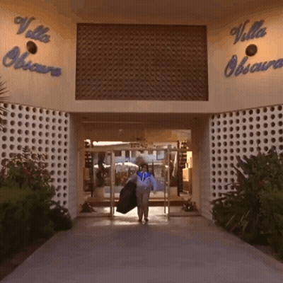 A Woman Carrying A Jacket Walks Into The Villa Obscura Building GIF