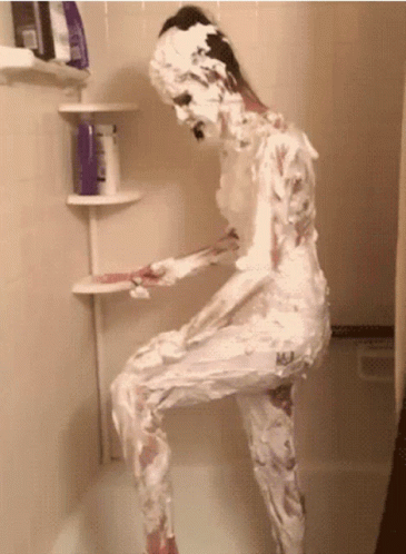 A Woman Covered In Shaving Cream Stands In A Shower GIF
