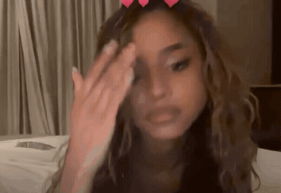A Woman Covering Her Face With Her Hand And A Heart On Her Head GIF