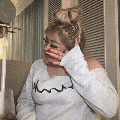 A Woman Covering Her Face With Her Hand And Wearing A White Shirt That Says Kmu GIF
