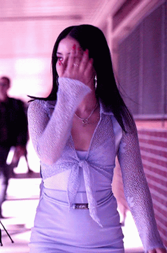 A Woman Covering Her Face With Her Hand In Front Of A Brick Building GIF