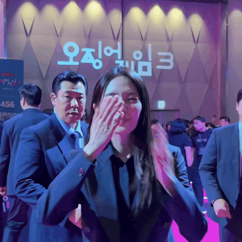 A Woman Covering Her Face With Her Hand In Front Of A Sign That Says 456 GIF