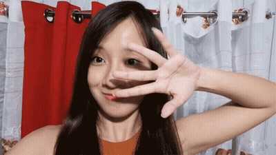 A Woman Covering Her Face With Her Hand In Front Of Red Curtains GIF