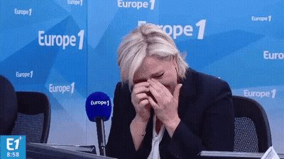 A Woman Covering Her Face With Her Hands In Front Of A Europe 1 Banner GIF