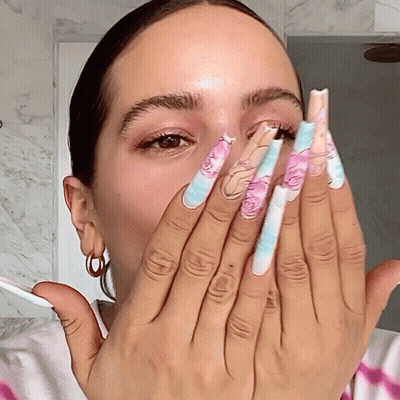 A Woman Covering Her Face With Her Hands With Long Nails With A Floral Design On Them GIF