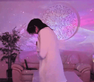 A Woman Dancing In A Living Room With Purple Lights GIF