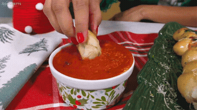 A Woman Dipping A Piece Of Bread Into A Bowl Of Sauce GIF