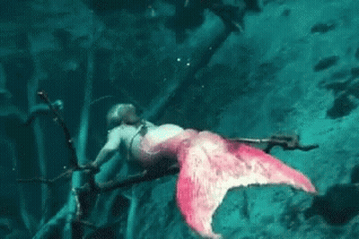 A Woman Dressed As A Mermaid Is Swimming In The Ocean With A Sword . GIF