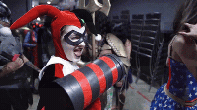 A Woman Dressed As Harley Quinn Is Holding A Red And Black Striped Object GIF