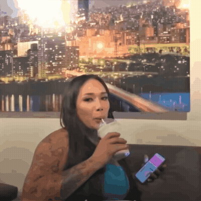 A Woman Drinking A Milkshake While Holding A Phone That Says ' I Love You ' On It GIF