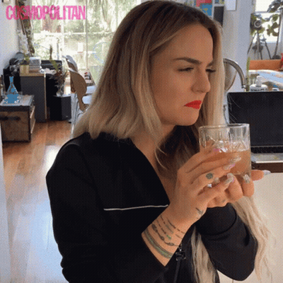 A Woman Drinking From A Glass With Cosmopolitan Written On The Bottom Right GIF