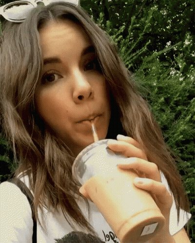 A Woman Drinking Through A Straw From A Cup That Says ' Iced Tea ' On It GIF