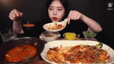 A Woman Eating A Plate Of Food With A Spoon In Her Mouth GIF