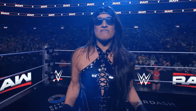 A Woman Flexes Her Muscles In Front Of A Wrestling Ring That Says ' Wwe ' On It GIF