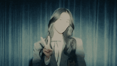 A Woman Giving A Peace Sign In Front Of A Curtain GIF