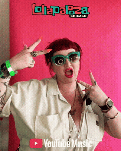 A Woman Giving A Peace Sign In Front Of A Sign That Says ' Lollapaloza Chicago ' GIF