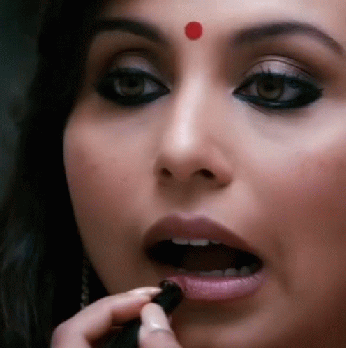 A Woman Has A Red Dot On Her Forehead And Is Applying Lipstick GIF