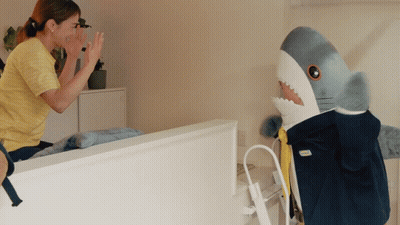 A Woman High Fives A Stuffed Shark That Is Wearing A Ikea Jacket GIF